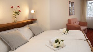 Une chambre d’hôtel avec un grand lit, deux oreillers, une table de chevet ornée d’un vase de fleurs, une chaise et une fenêtre avec des rideaux.