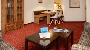 Un salon chaleureux avec un meuble en bois, une table à manger avec des chaises et un sol recouvert d’une moquette rouge.