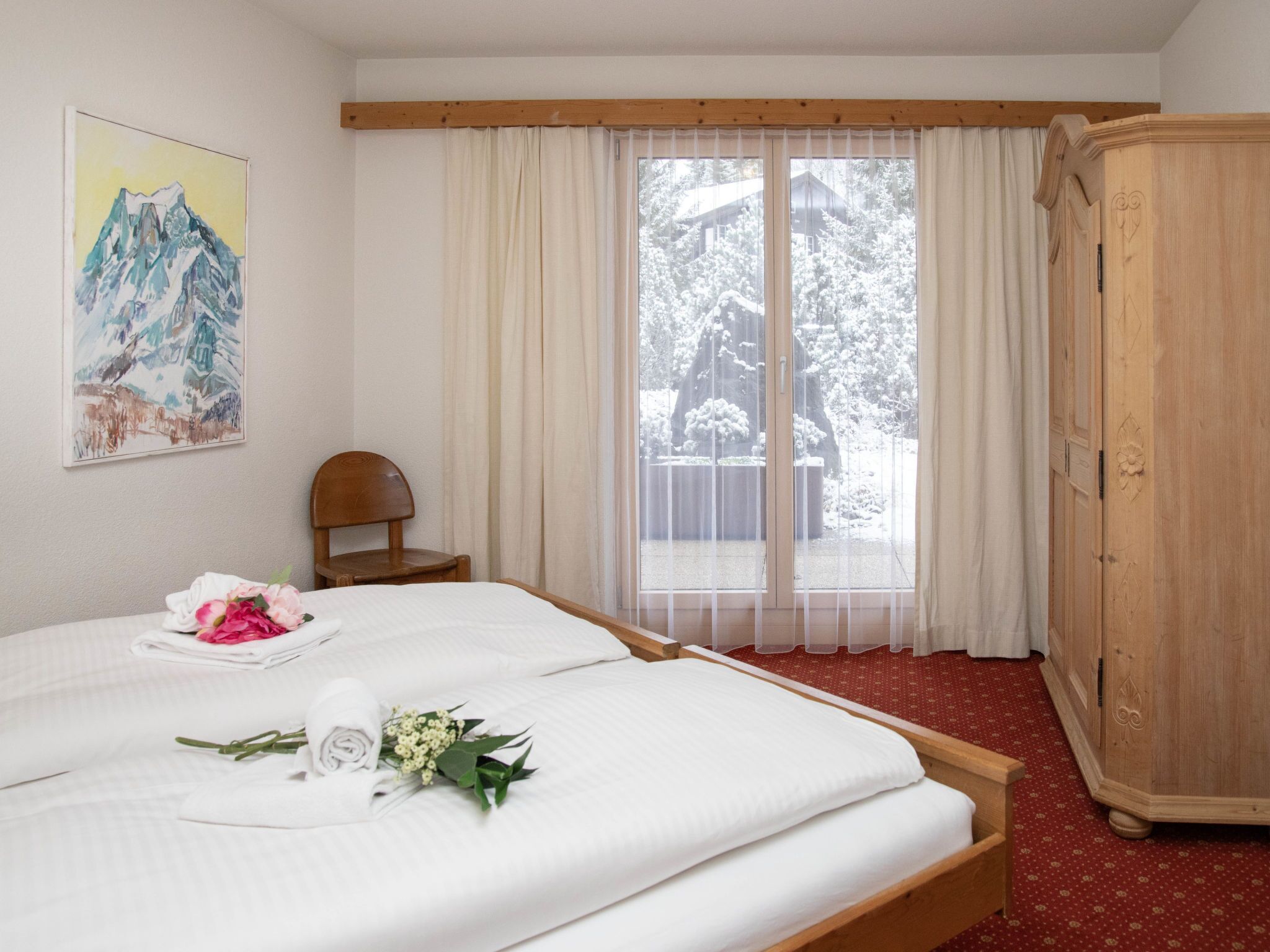 A hotel room with a bed, a wooden wardrobe, a chair, and a painting on the wall.