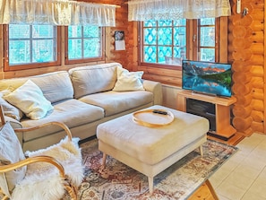 Un salon chaleureux avec un canapé, un pouf et un téléviseur fixés à un mur en bois.