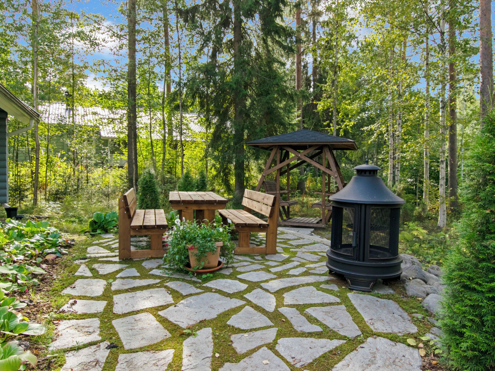 A stone patio with wooden furniture, a wooden swing set, and a black lantern.