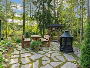 Une terrasse en pierre avec des meubles en bois, une balançoire en bois et une lanterne noire.