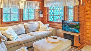 Ein gemütliches Wohnzimmer mit einer Couch, einem Hocker und einem Fernseher auf einem Holzboden.