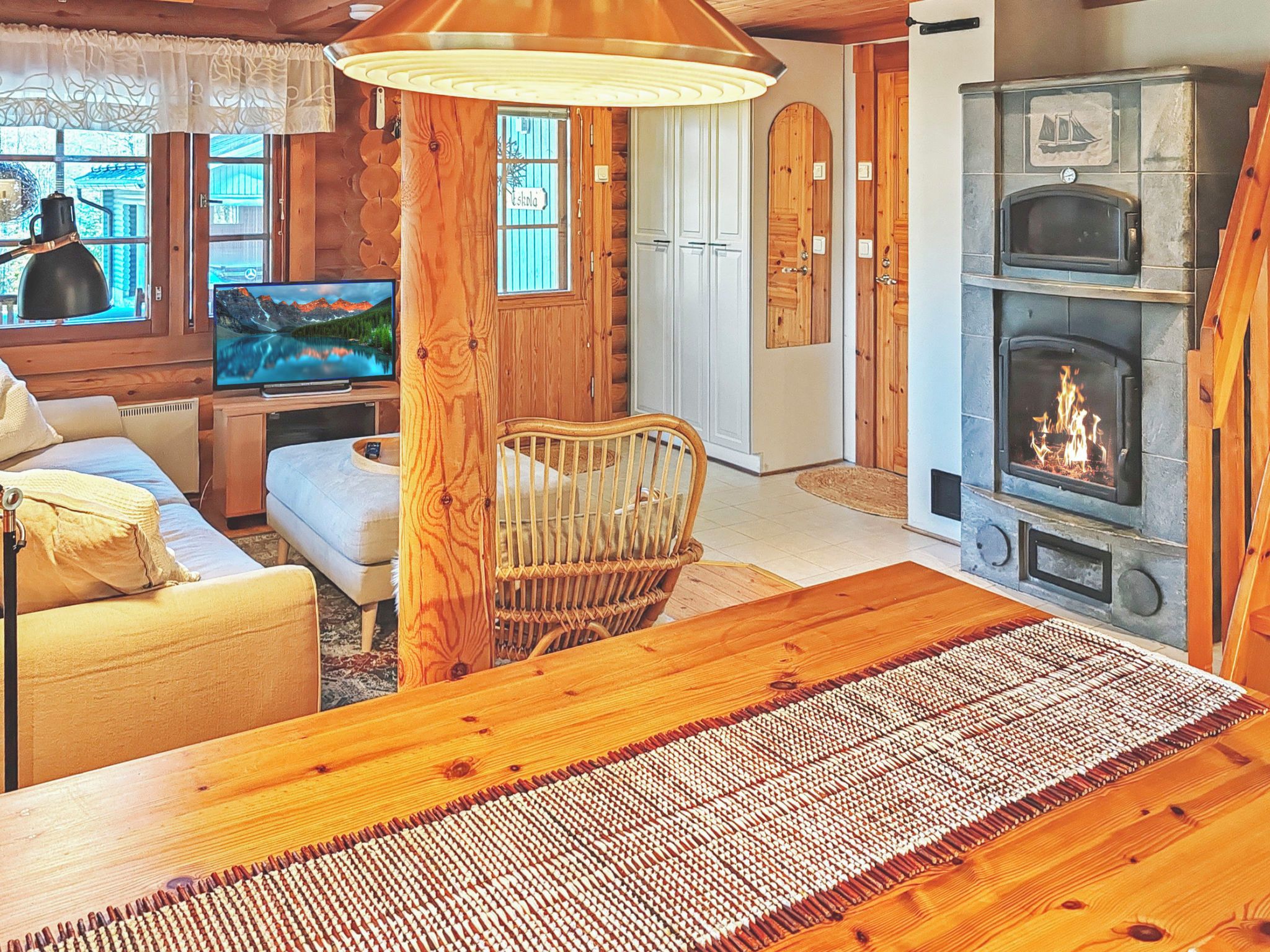 Un interior cálido de cabaña con una mesa de comedor de madera, un televisor, una chimenea y una silla de mimbre.