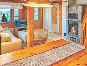 L’intérieur chaleureux d’un chalet avec une table à manger en bois, un téléviseur, une cheminée et un fauteuil en osier.