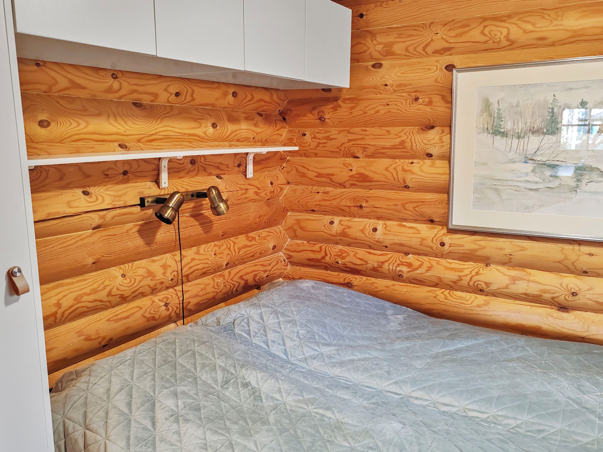Esquina de una habitación con paredes de madera, un armario blanco, una estantería y un colchón.