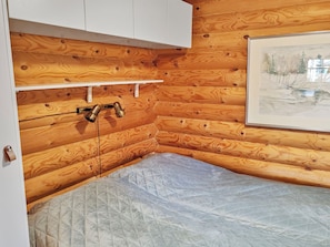 Un coin de pièce aux murs en bois, avec une armoire blanche, une étagère et un matelas.