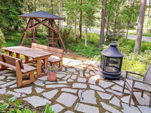 An outdoor patio with a swing set, wooden table and benches, a potted plant, and a lantern.