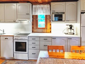 A compact kitchen with white cabinets, a stove, a microwave, and a coffee maker.