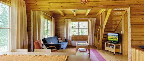 Interior de una cabaña de madera con sofá, una mesa y televisor.
