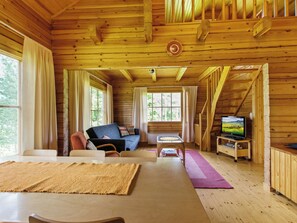 Interior de una cabaña de madera con sofá, una mesa y televisor.