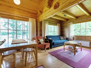 A wooden cabin interior with a dining table, chairs, a sofa, and a coffee table.