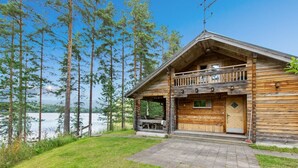 Een houten blokhut met balkon, een pad van stenen en uitzicht op een meer omgeven door bomen.