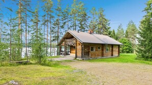 Een vakantiehuisje van hout met een veranda, omringd door hoge bomen en een gazon.