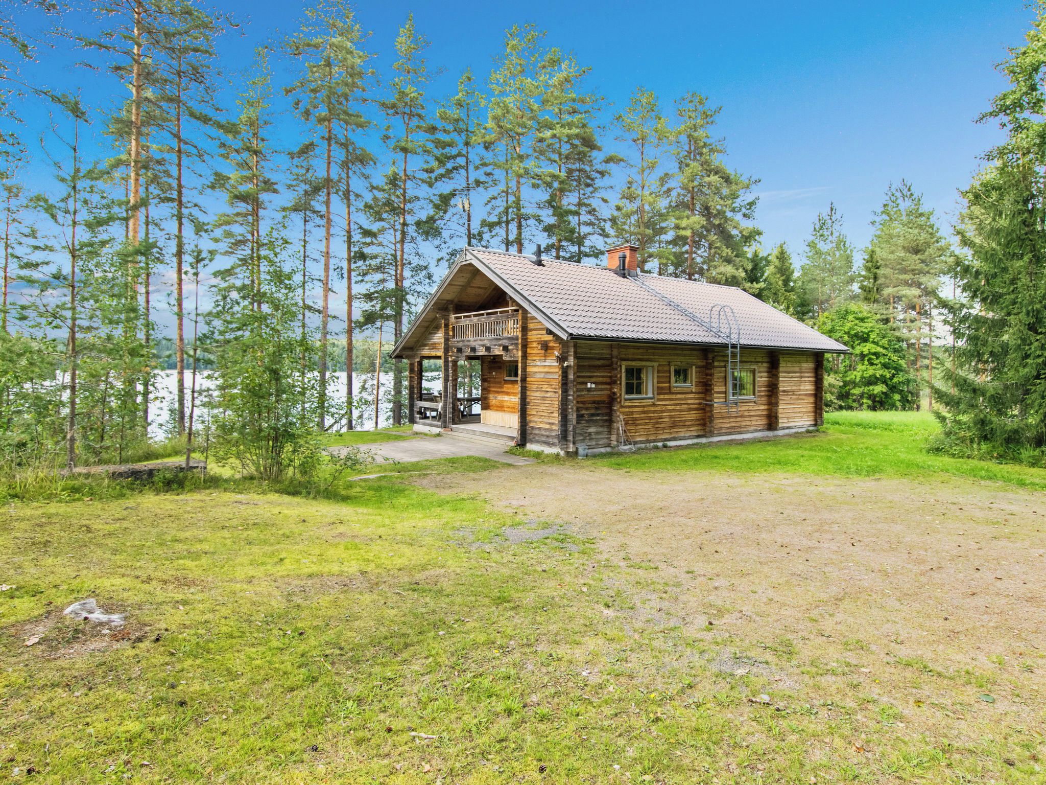 Puinen mökki, jossa on kuisti, ja sen ympärillä on nurmikkoalue sekä korkeita puita.