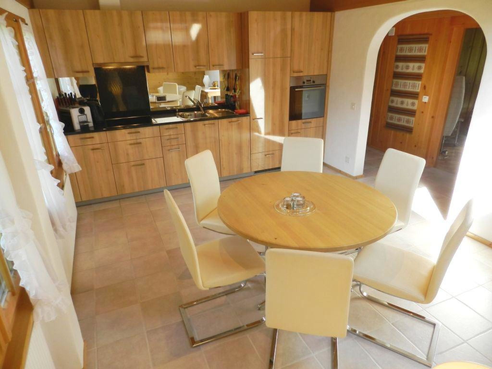 Een moderne keuken met houten kastjes, een ronde eettafel met stoelen en een inbouwoven.