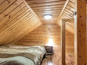 Une chambre mansardée en bois, avec un plafond en pente, un lit simple, une table de chevet et une petite table.