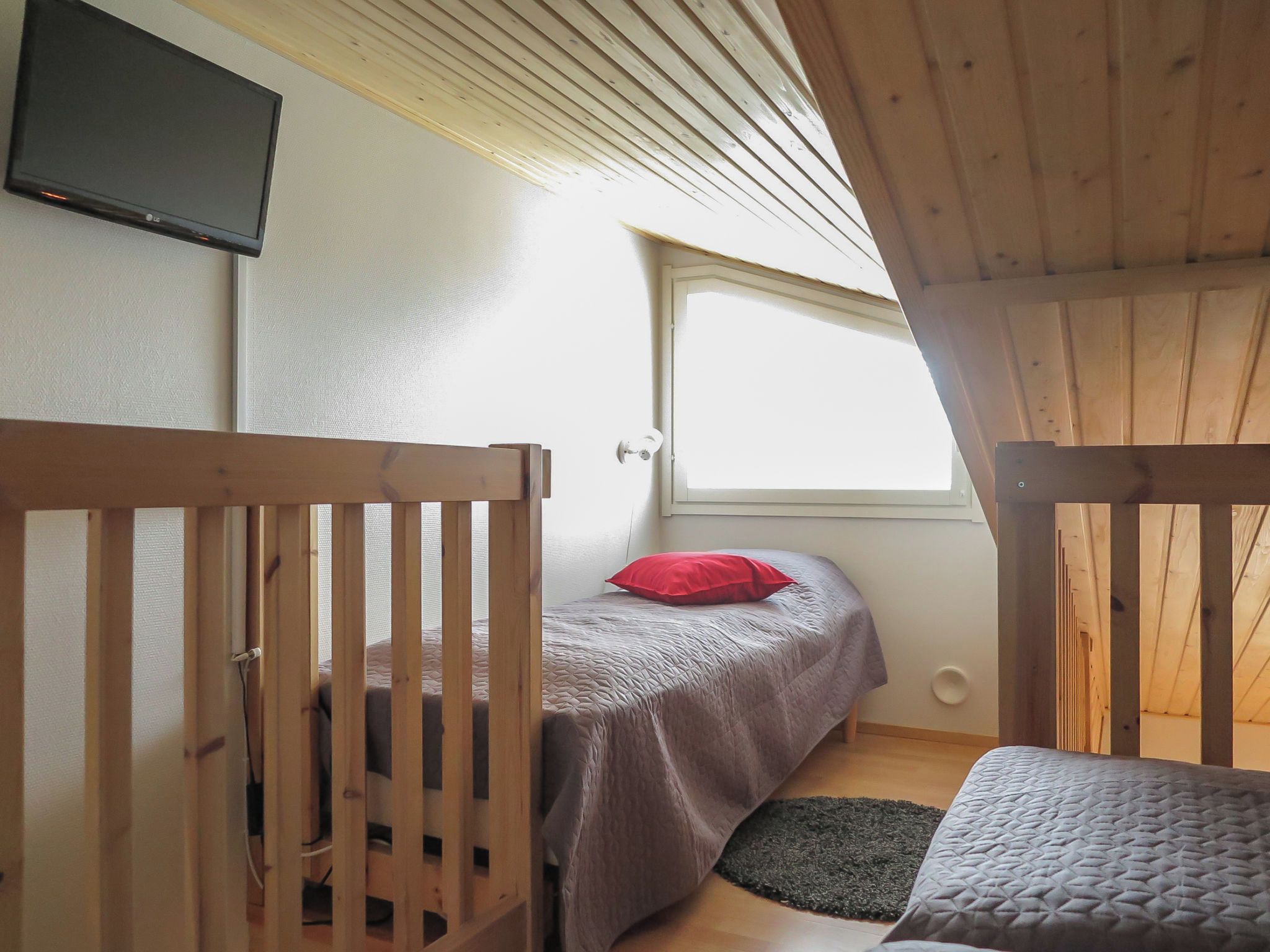 A bedroom with a bed, a window, and a TV mounted on the wall.
