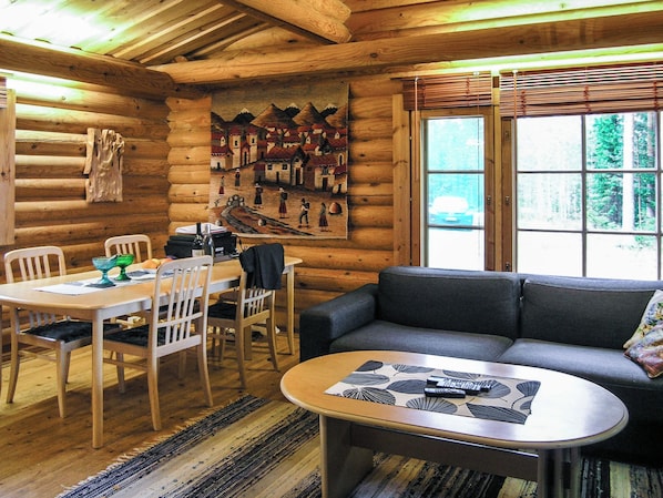Et interiør af en hytte med spisebord, stole, sofa og et vindue med persienner.