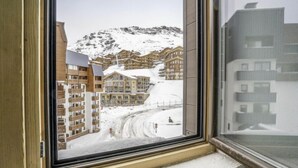 Uitzicht vanuit een raam op een besneewd berglandschap met gebouwen, waaronder een skigebied en woonhuizen.