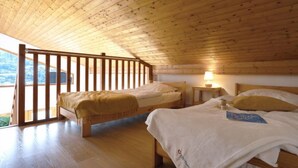Acogedor dormitorio en ático con pisos de madera y techo inclinado, con dos camas y una mesita con lámpara.