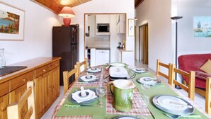 Un comedor con una mesa de madera dispuesta para cuatro, una cocina al fondo y un sofá rojo.