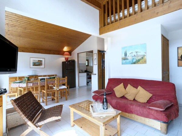 A cozy living area with a red sofa, wooden furniture, and a dining table.