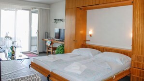 Et hotelværelse med en seng, et skrivebord med en computer, en stol og et vindue med gardiner.