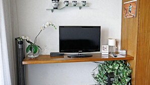 Et moderne værelse med et træskrivebord, et fladskærms-tv, en lille plante og en hylde med pynt.