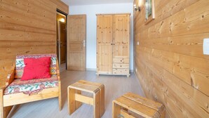 A wooden room with a sofa, two small stools, and a wardrobe. - Arcelle 203 by Interhome (Val Thorens)