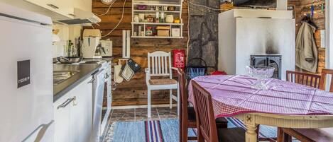 A rustic kitchen with a stone floor, wooden walls, and a dining area with a checkered tablecloth.