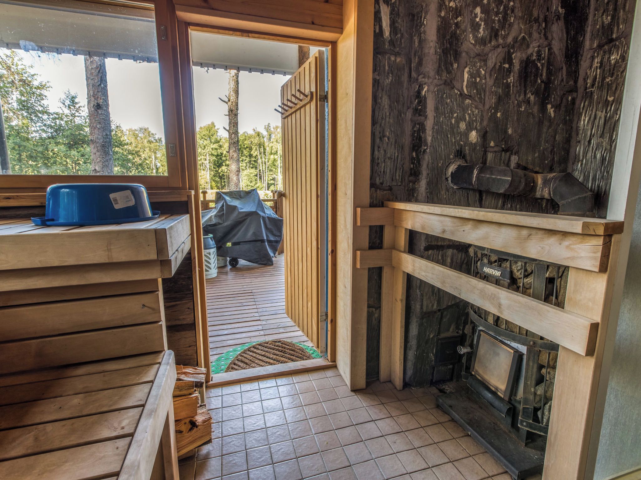 Interior de madera con chimenea, un banco y una puerta que da al exterior.
