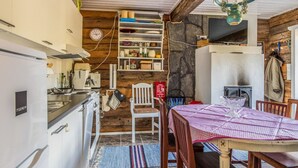 A kitchen with white cabinets, a stove, and a sink. There is a wooden dining table with chairs and a rug. - Vacation home Björn by Interhome (Kemiönsaari)