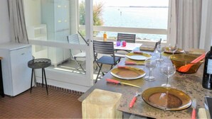 A dining area with a view of the sea, a table set with plates, glasses, and cutlery, and a refrigerator in the corner. - Les Occitanes by Interhome (Gruissan)