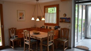 Un comedor con mesa y sillas de madera, una araña y una ventana con vistas a zonas verdes.