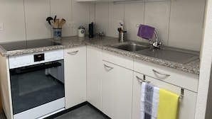 A kitchen with white cabinets, a granite countertop, a built-in oven, a sink, and a microwave. - Apartment Hari by Interhome (Adelboden)
