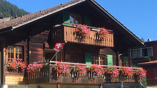 A wooden chalet with a balcony adorned with flowers and a Swiss flag. - Apartment Hari by Interhome (Adelboden)