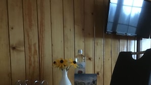 A wooden dining table with a vase of sunflowers, a bottle, and a card. There are two black chairs and a television mounted on the wall. - Apartment Hari by Interhome (Adelboden)
