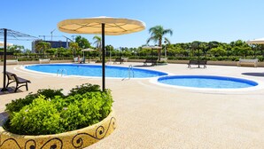 Un área de piscina con dos piscinas circulares, rodeada de sillones de descanso y sombrillas.