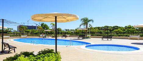 A pool area with two circular pools, surrounded by lounge chairs and umbrellas.