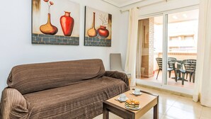 Un salón con un sofá marrón, una pequeña mesa con un plato de pasteles, y dos cuadros de jarrones en la pared.