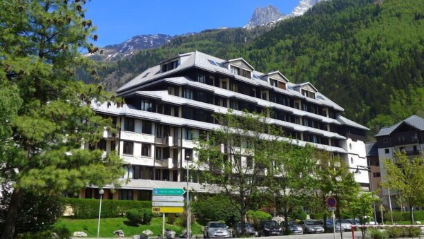 Un hôtel à plusieurs étages, doté d’une architecture moderne, situé dans une région montagneuse où l’on aperçoit les sommets au loin.