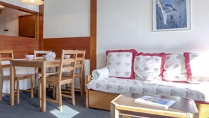 Une pièce chaleureuse avec une table à manger en bois, des chaises, un canapé agrémenté de coussins à motifs, une petite table sur laquelle repose un livre et un tableau accroché au mur.