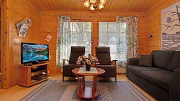 A cozy cabin interior with a television, two chairs, a sofa, and a small table with flowers.