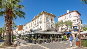 Ein öffentlicher Platz mit Straßencafés, Palmen und historischen Gebäuden.