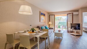 Ein modernes Wohnzimmer mit Essbereich, einer Couch, einem Fernseher und einem Balkon mit Gartenmöbeln.