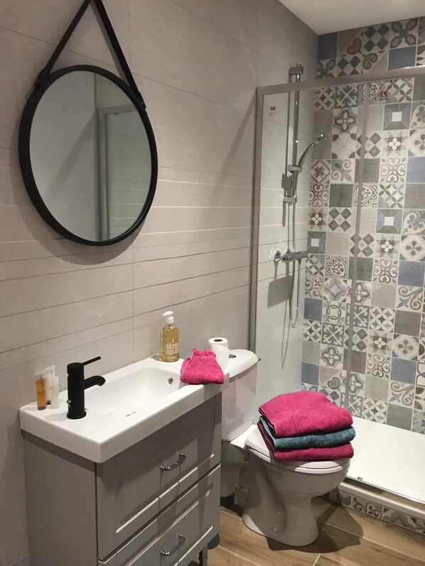 Un baño con lavamanos blanco, espejo, inodoro y ducha.