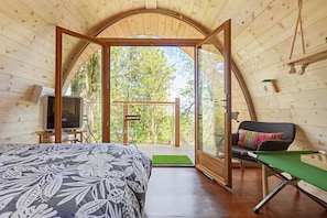 Una habitación acogedora con una cama, un televisor, una mesa con un tablero de ajedrez y vistas a árboles a través de un arco abierto.