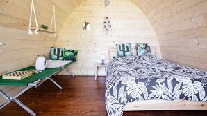 A cozy, wooden interior with a curved ceiling, a bed with floral bedding, a small table with a chessboard, and a hanging light fixture. - Monchateau étoilé Hébergement insolite (Merlas)