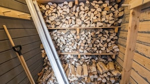 Un área de almacenamiento con estantes llenos de leña y una escalera metálica apoyada en la pared.